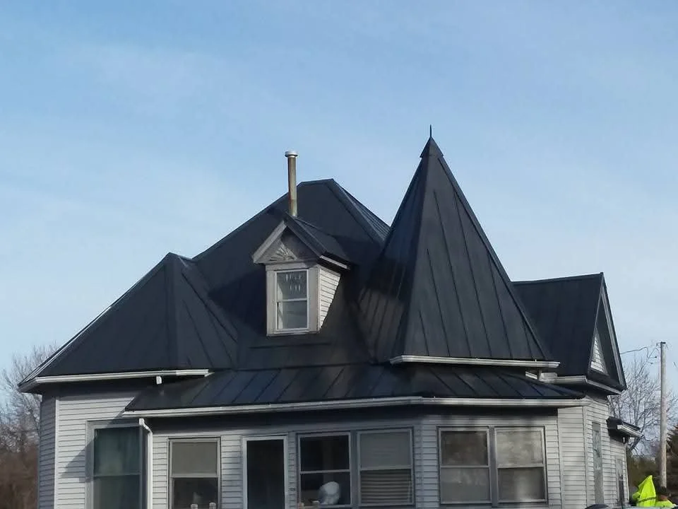 Black standing seam metal roof with dormers and chimney on white vinyl sided house