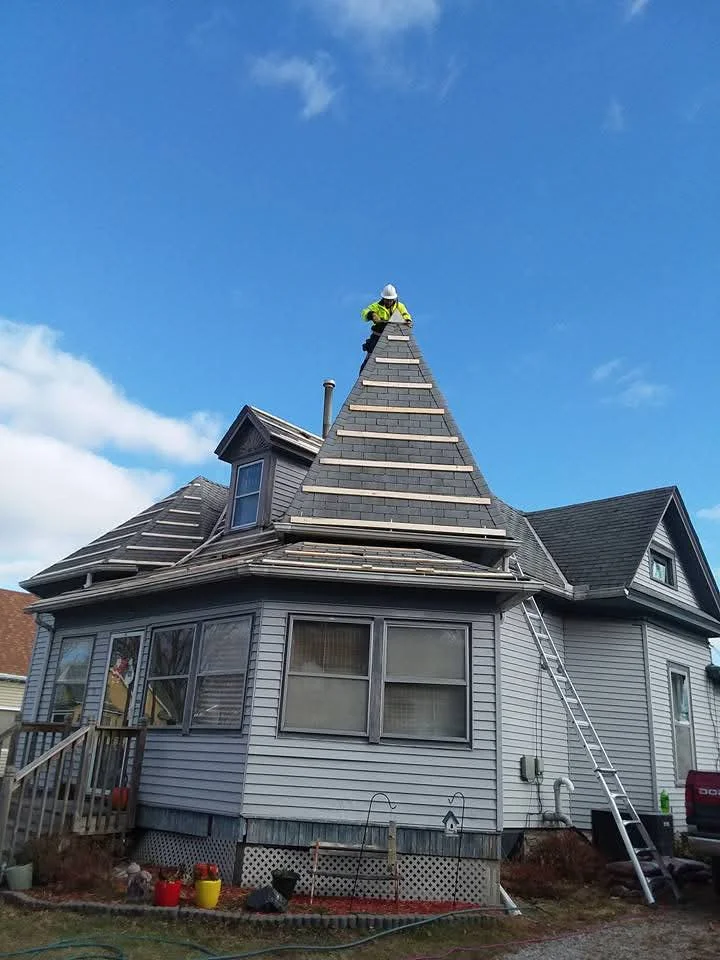 Roofer installing slate architectural shingles on Victorian turret roof with dormers