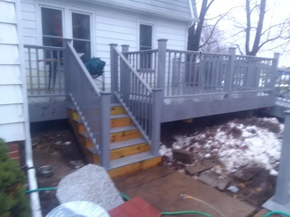 Elevated composite deck with gray railings, yellow stairs, and vinyl siding on residential home
