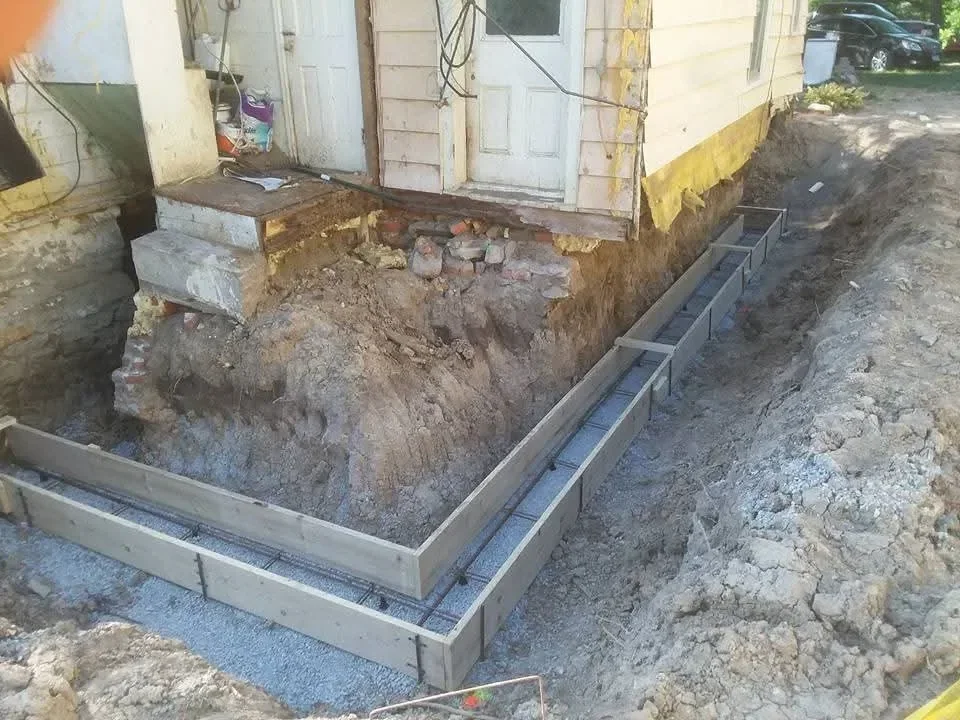 Metal drainage gutter installation with excavated soil and gravel base preparation at foundation