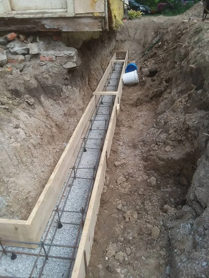 Excavated foundation trench with wooden forms, rebar reinforcement, and gravel base preparation