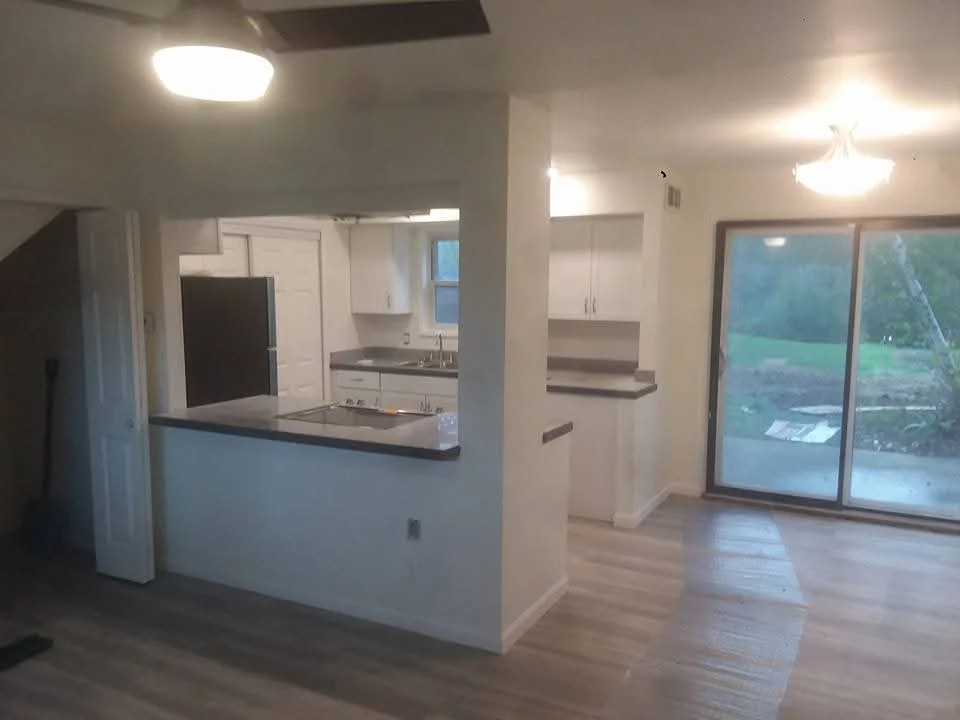 Modern kitchen with white cabinets, dark countertops, and hardwood flooring in open-concept layout