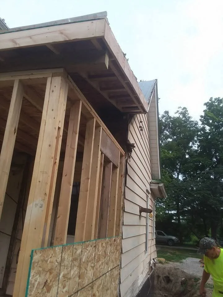 Wooden roof framing with exposed trusses, soffit construction, and plywood sheathing during installation