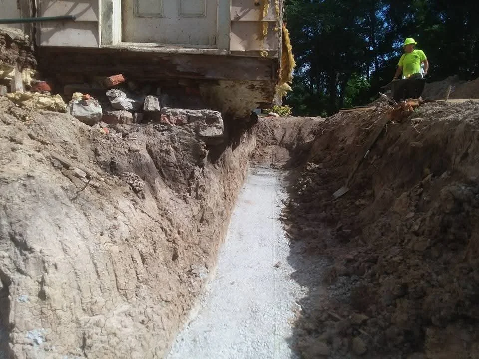 Excavated trench with exposed foundation and drainage work, clay soil walls