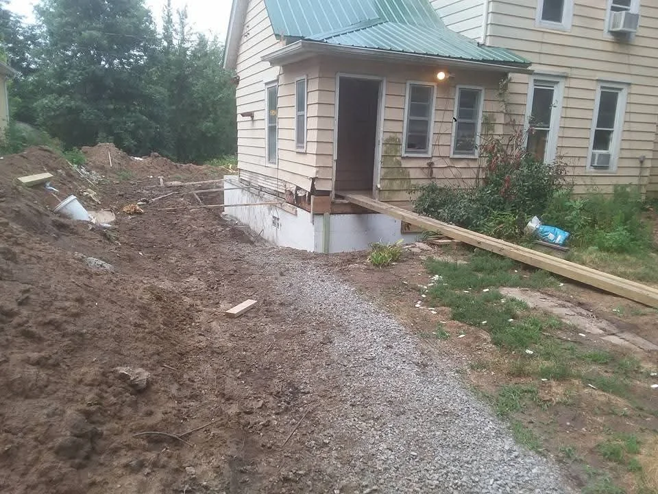 Excavated foundation area with gravel base and wooden retaining boards beside residential home